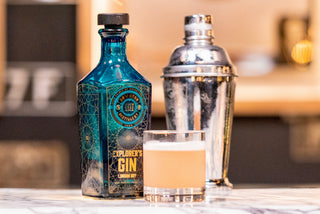 Explorer's Gin bottle with a cocktail shaker and glass on a blurred background