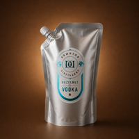 A silver stand-up pouch of Hazelnut Vodka, featuring a white and teal label, set against a warm brown gradient background.