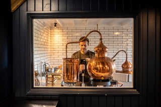Person working with copper stills in a distillery setting