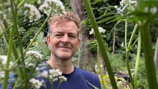 Man standing among green plants and white flowers