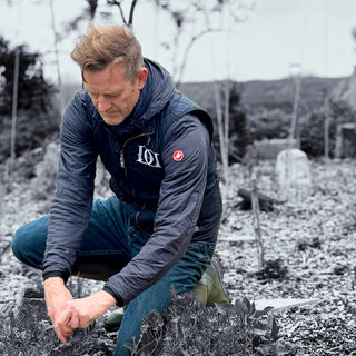 Hugh Anderson in a blue jacket with a logo tending to plants outdoors