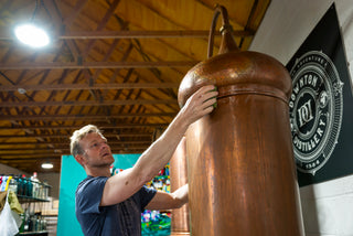 Man interacting with a large copper still in a distillery setting