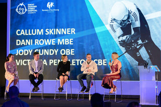 Panel discussion with speakers on a stage in front of a large screen displaying names and images.